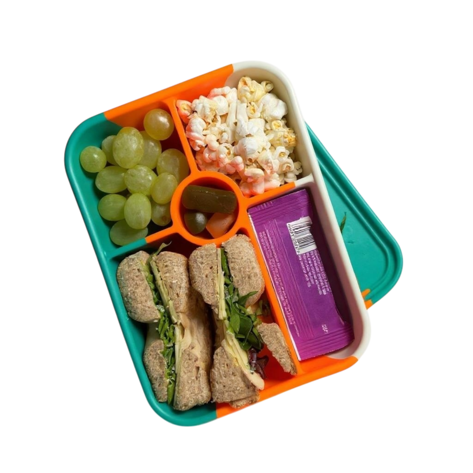 An overhead view of an open 5-compartment silicone kids bento box packed with sandwiches, grapes, popcorn, and snacks.