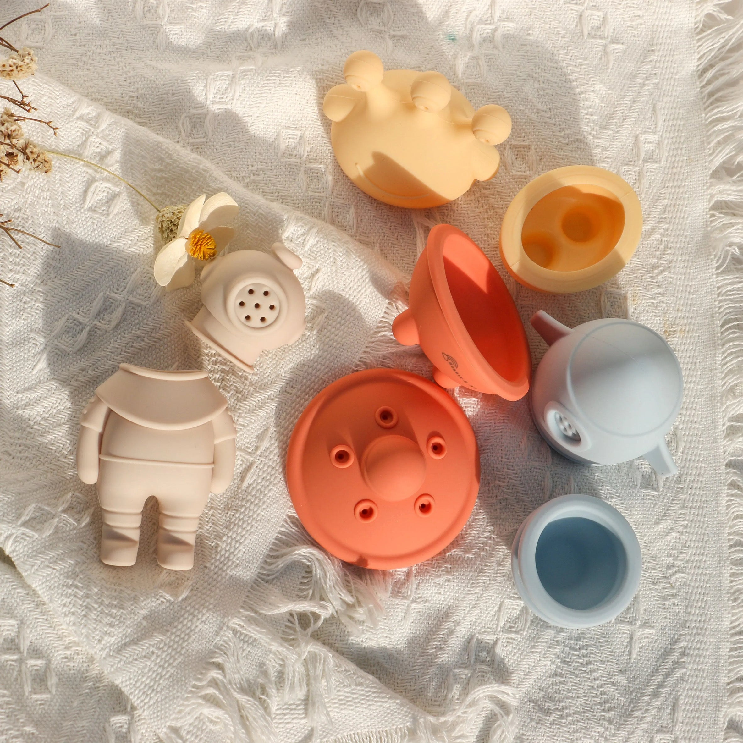 Bumble & Ivy detachable silicone bath toys shown separated into halves on a white blanket, highlighting the hygienic, open design for thorough cleaning and drying.