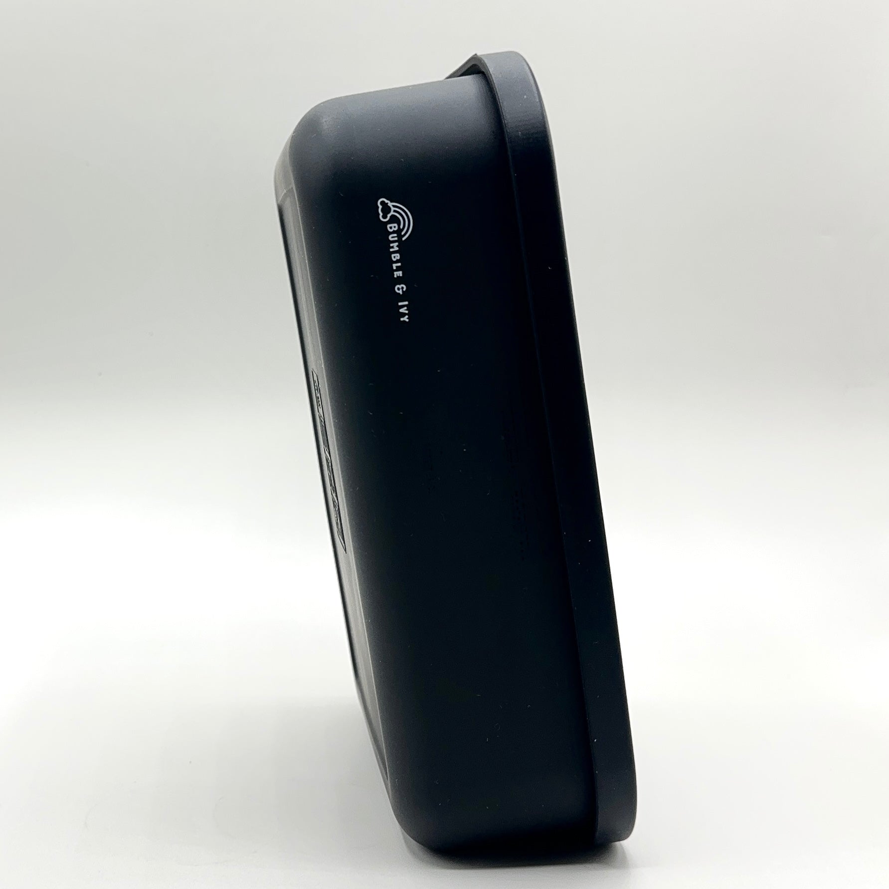 Side profile view of the closed Bumble & Ivy midnight black silicone bento box standing upright on a white background, highlighting the slim design and white engraved brand logo.
