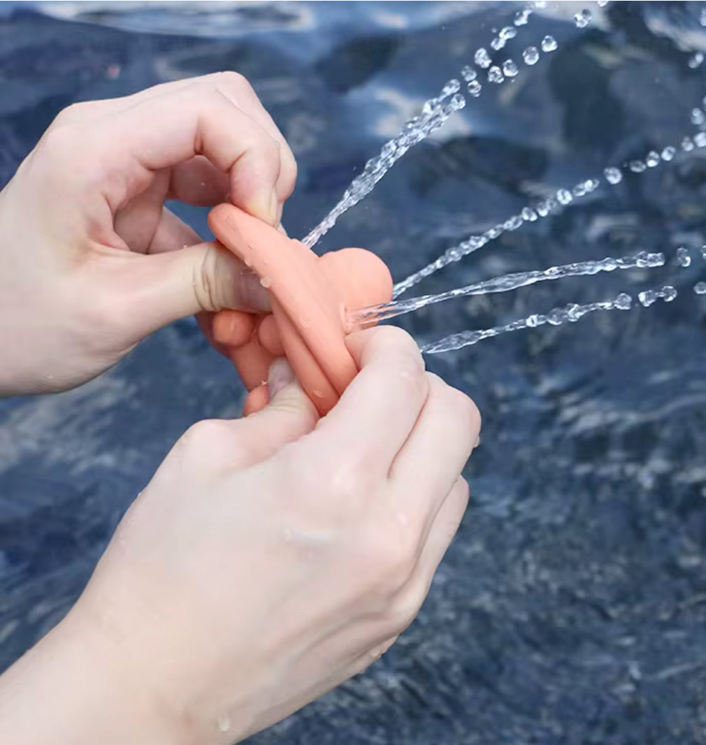 Hands squeezing a peach UFO silicone squirt toy in water to show how these easy-clean bath toys still spray water perfectly without the risk of trapped mould.